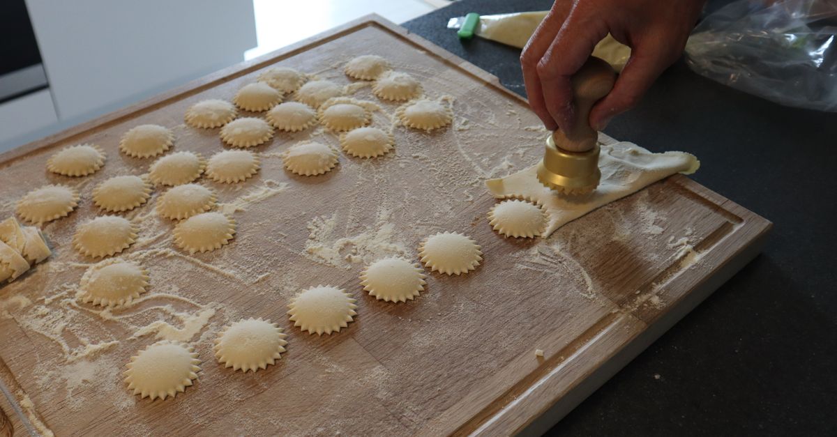 Person making homemade ravioli with a pasta cutter on a floured wooden board.